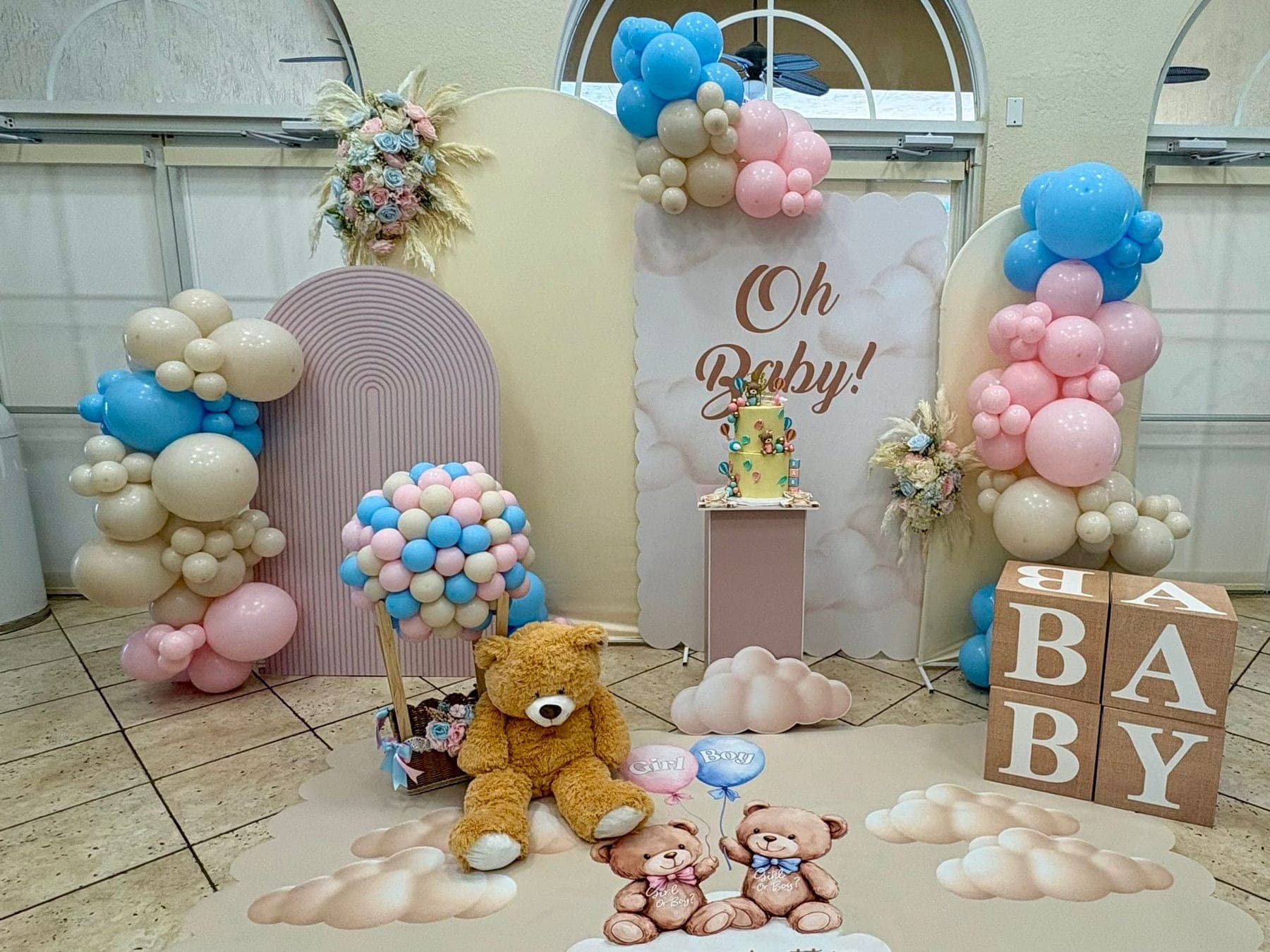 Pink and blue gender reveal scene with 'Oh Baby' backdrop, balloon columns, BABY blocks and teddy bear